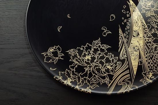 Jet black plate with a gold climbing peacock makie design, close-up of the design
