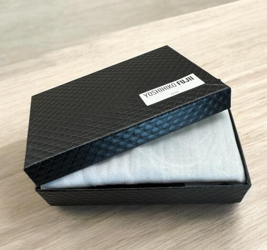 Black textured gift box with the lid partly open, plate wrapped inside